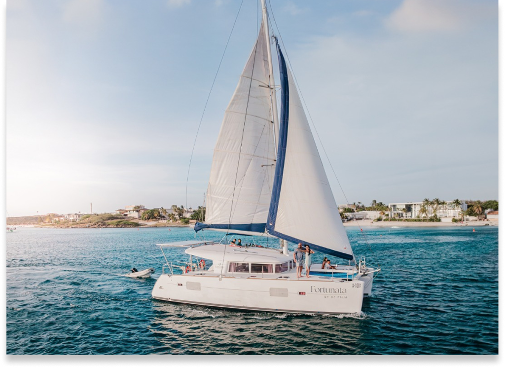 Sailboat with white sails on the ocean near a coastline on a sunny day.